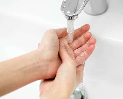 Hands being washed under a faucet with clear water on a white background